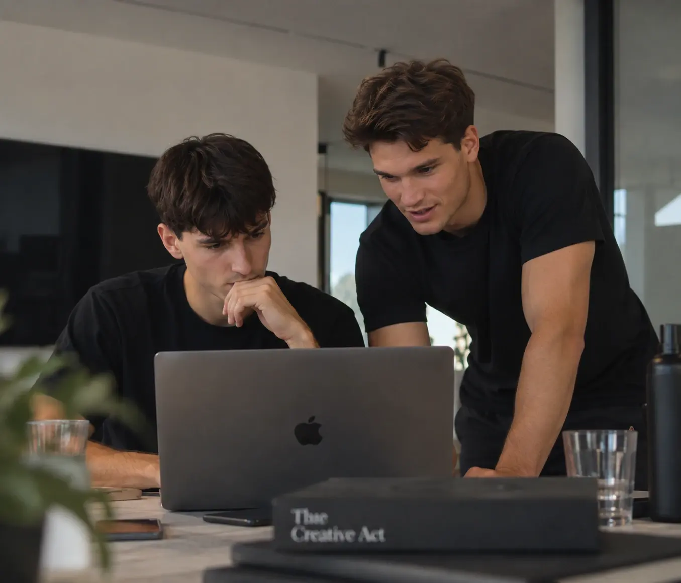 Tom und Ruben beugen sich gemeinsam über einen Laptop und besprechen ein Webprojekt.